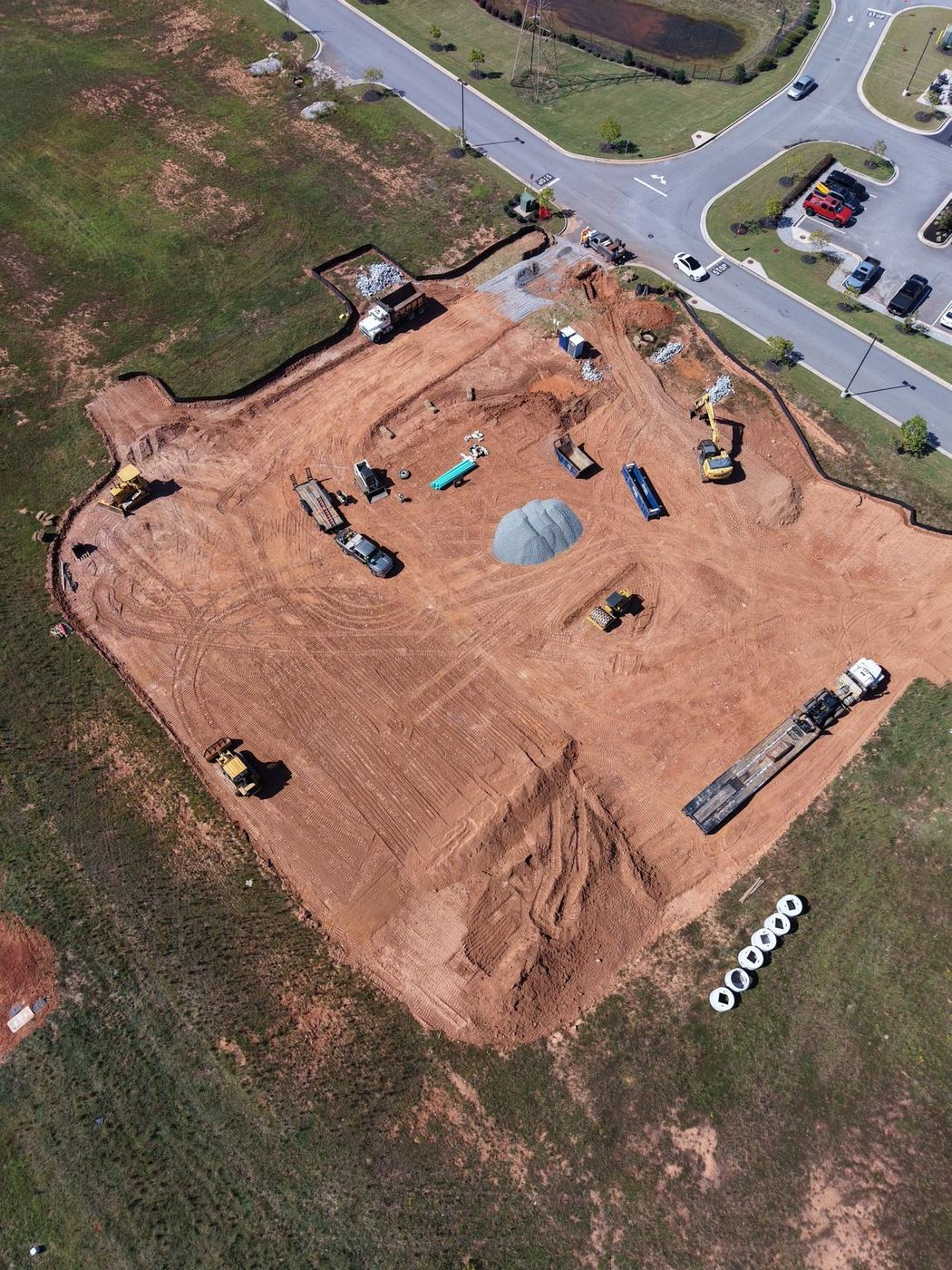 Aerial view of a commercial pad being graded, with silt fence, stone, and equipment