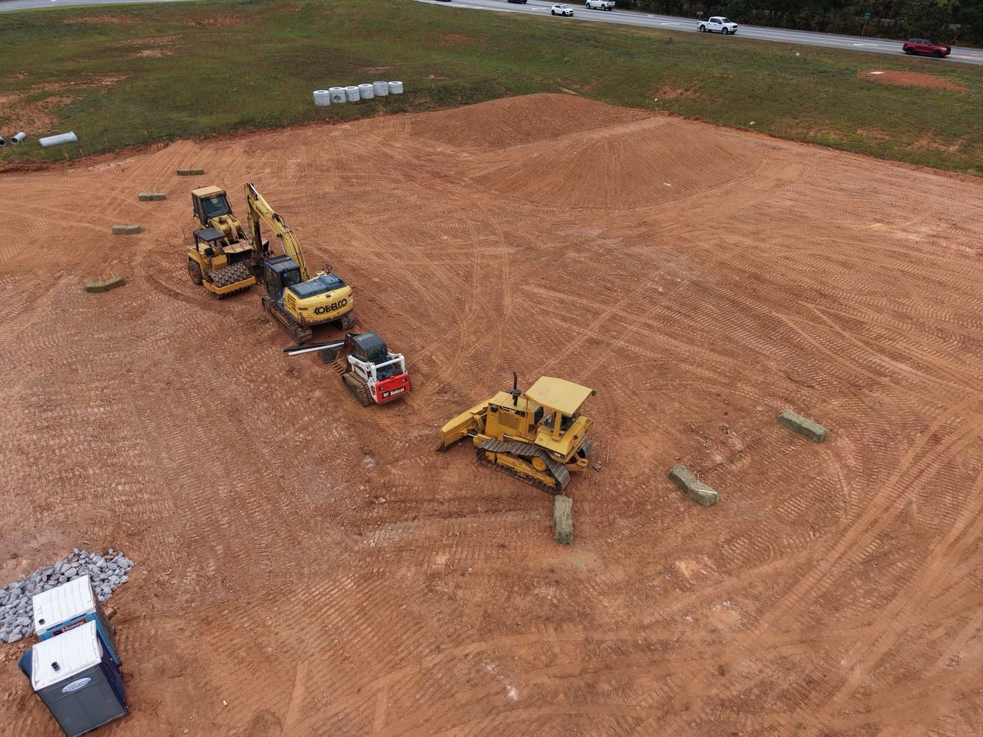 Aerial view of a dozer, excavator, compactor, and skid steer on a graded pad