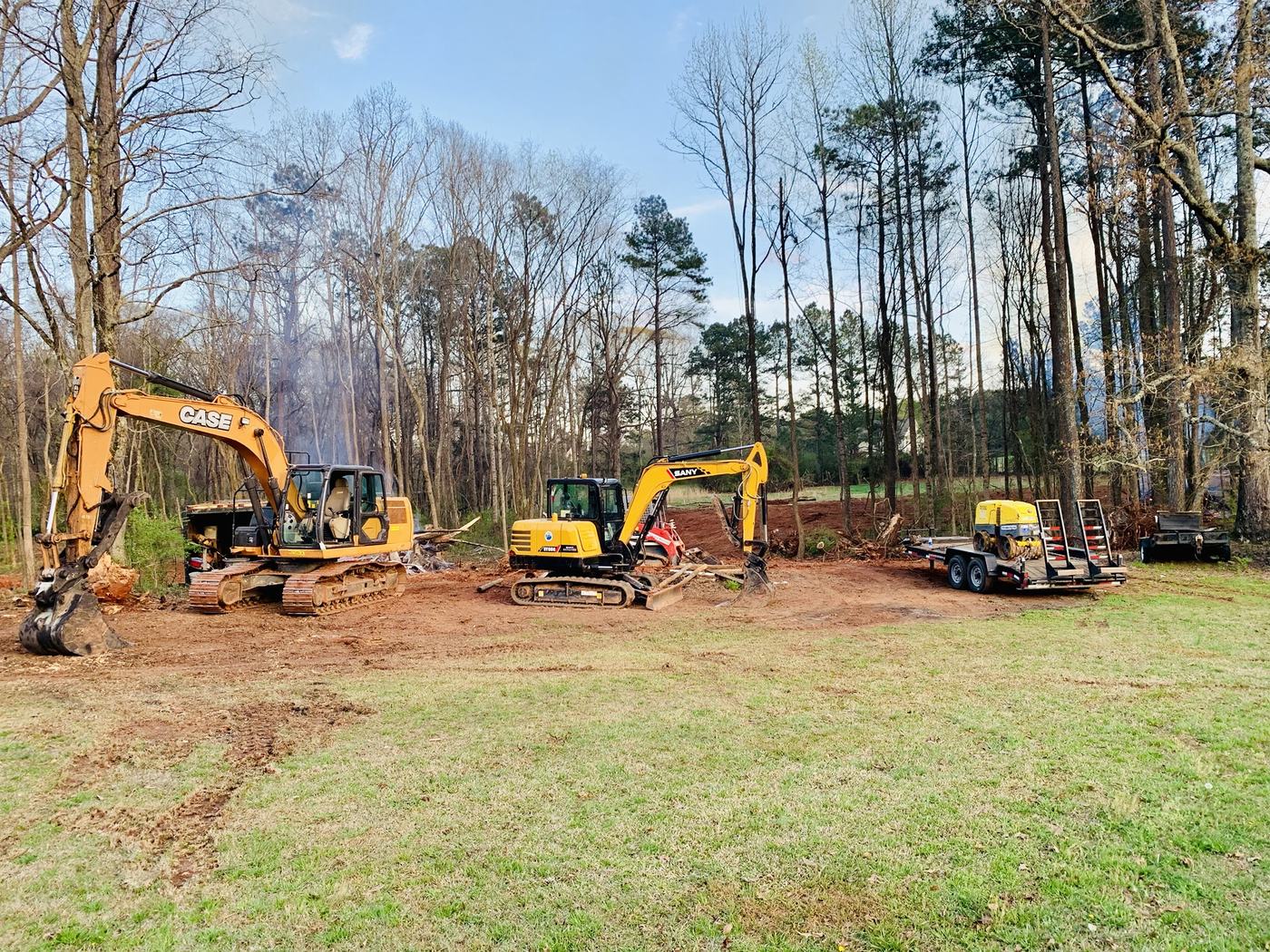 Case and Sany excavators with a compactor trailer on a clearing job