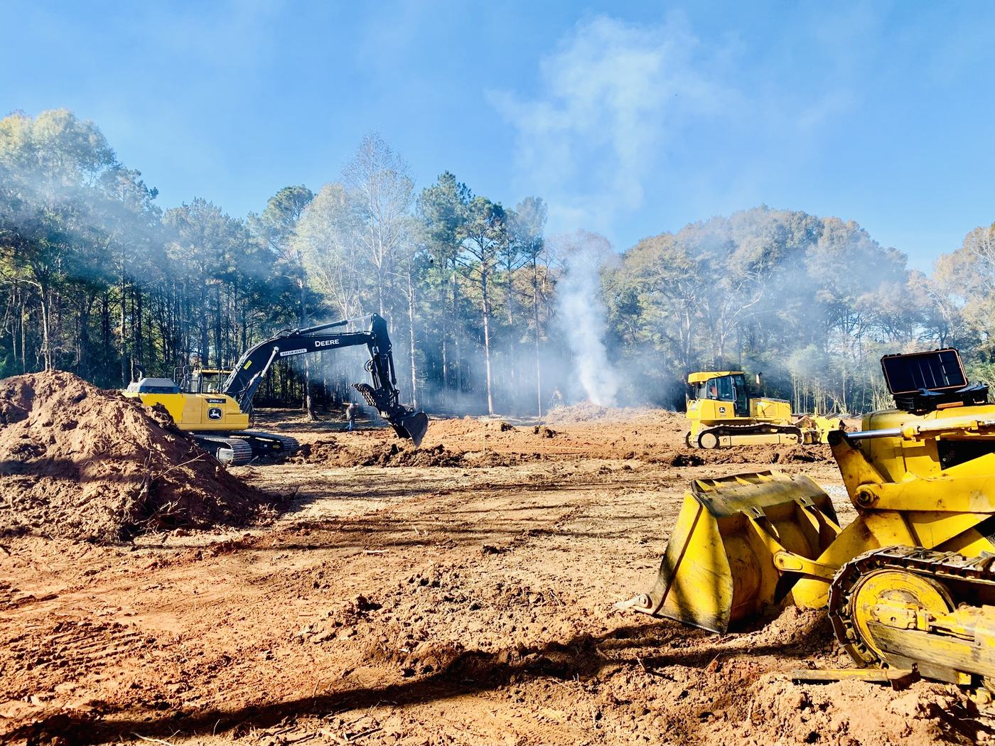 Deere excavator and dozer stripping a site while debris burns