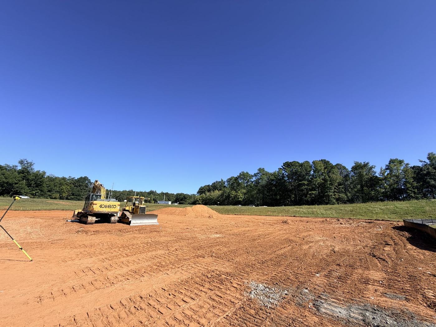 Wide view of a graded pad with excavator and dozer