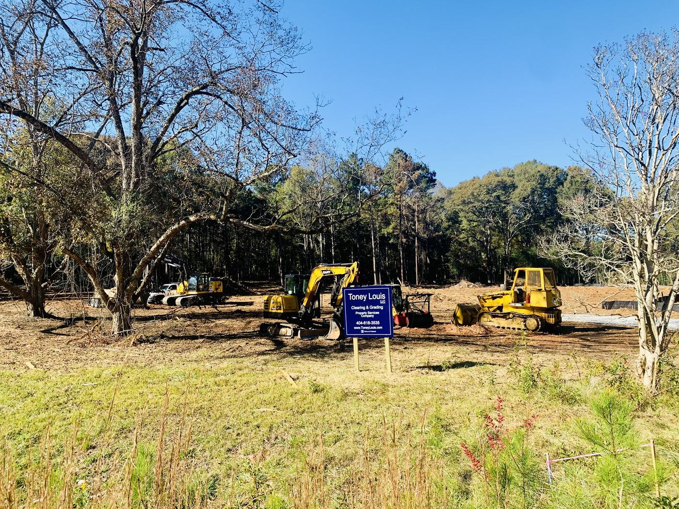 Toney Louis job sign in front of excavators, a mulcher, and a dozer on a cleared lot
